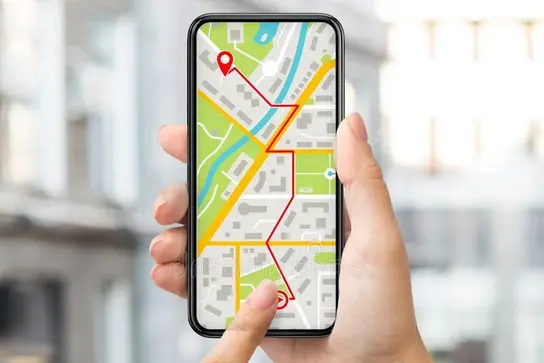 Eine Hand hält ein Smartphone, auf dessen Bildschirm eine Kartenansicht mit verschiedenen Straßen und markierten Punkten angezeigt wird. Eine Fingerberührung deutet auf eine Position auf der Karte hin.