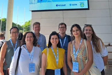 Eine Gruppe von sieben Personen steht lächelnd vor einem großen digitalen Banner, das Informationen über den 6. Europäischen Kongress für Medizinische Physik 2026 zeigt. Das Banner betont die Themen Gesundheitsversorgung durch Physik und die Verbindung von Wissenschaft und Patientenversorgung.