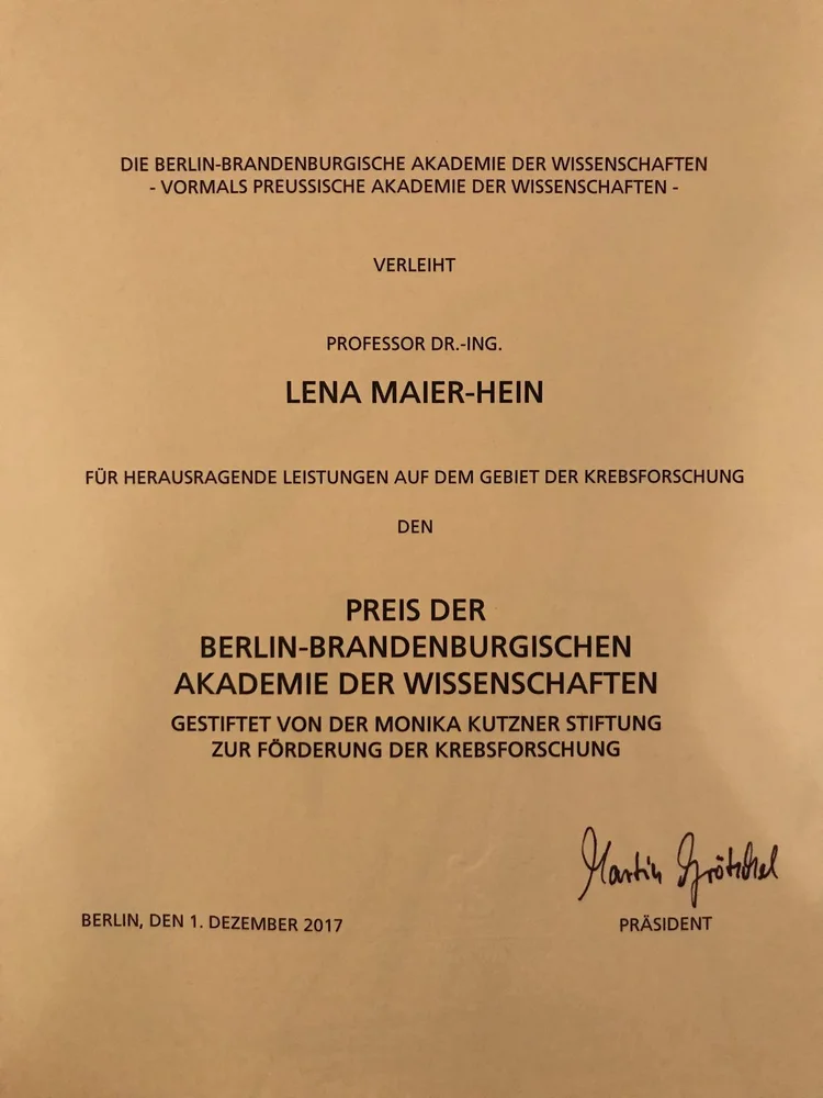 Certificate awarded by the Berlin-Brandenburg Academy of Sciences to Professor Dr.-Ing. Lena Maier-Hein for outstanding achievements in cancer research. The award is supported by the Monika Kutzner Foundation for cancer promotion. The document is dated December 1, 2017, and includes a handwritten signature.