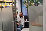 Zwei Personen sitzen in einem modernen Beratungsraum. Eine Frau in einem weißen Kittel bespricht Dokumente mit einem Mann. Im Hintergrund sind Bücherregale mit Informationsmaterialien zu sehen.