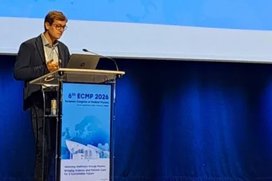Ein Mann spricht auf einer Bühne bei einer Konferenz. Er steht an einem Rednerpult mit einem Laptop und zeigt eine Präsentation. Auf dem Bildschirm sind Informationen über ihn und das Deutsche Krebsforschungszentrum angezeigt.