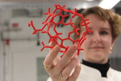 Eine Person hält ein rotes Molekülmodell in der Hand, das aus vielen miteinander verbundenen Strukturbausteinen besteht.