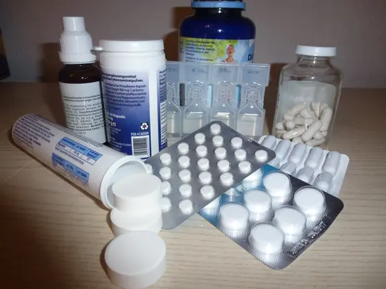 Eine Sammlung von Medikamenten und Nahrungsergänzungsmitteln auf einem Tisch. Dazu gehören verschiedene Pillenpackungen, Flaschen mit Tropfen und Pulver sowie Blisterpackungen mit Tabletten. Die Produkte sind in unterschiedlichen Größen und Formen angeordnet.
