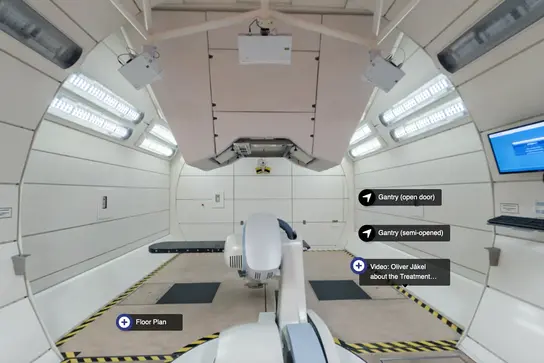 Das Bild zeigt den Innenraum einer modernen Strahlentherapie-Einrichtung. Im Zentrum steht ein Behandlungsgerät, umgeben von hellen Wänden und einer Decke mit Beleuchtung. Auf einer Wand sind Bildschirminformationen zu sehen, die Video- und Raumplanoptionen bieten.
