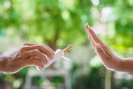 Eine Hand reicht eine Zigarettenschachtel in Richtung einer anderen Hand, die abwehrend ausgestreckt ist.