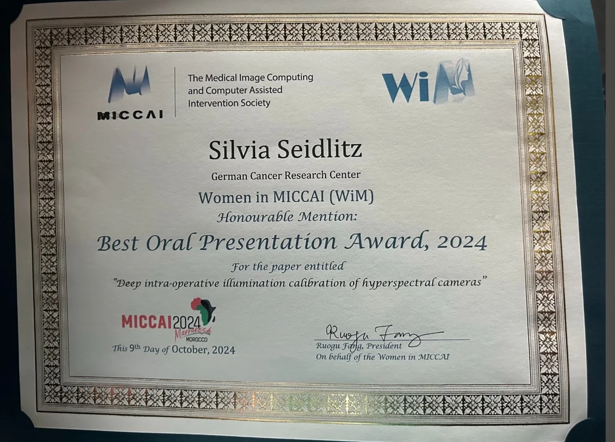 Certificate awarded to Silvia Seidlitz from the German Cancer Research Center, recognizing her for an Honorable Mention in the Best Oral Presentation Award at the MICCAI 2024 conference. The award is for her paper on the calibration of hyperspectral cameras.
