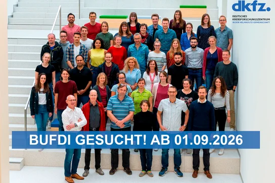 Gruppenfoto von 43 Personen auf einer Treppe, die vor einem hellen Hintergrund stehen. Einige Personen tragen unterschiedliche Kleidung. Im Vordergrund steht ein großer, blauer Text: "BUFDI GESUCHT! AB 01.09.2026".