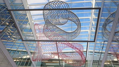 Eine moderne Kirchendecke mit skulpturalen, spiralförmigen Formen aus Metall und transparenten Elementen. Die Strukturen hängen beweglich in einem hellen Raum mit großen Fenstern, die Tageslicht hereinlassen und eine kreative Atmosphäre schaffen.