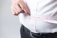 Ein Mann misst seinen Bauchumfang mit einem Maßband, das um seine Taille gewickelt ist.