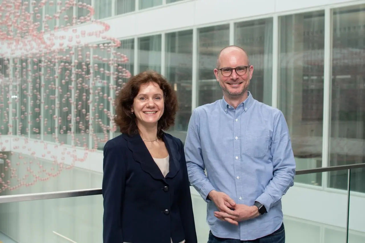Two professionals stand smiling together in a modern indoor setting. They appear to be discussing or collaborating on topics related to particle therapy, reflecting the focus of the surrounding educational content on advancing training in this medical field.