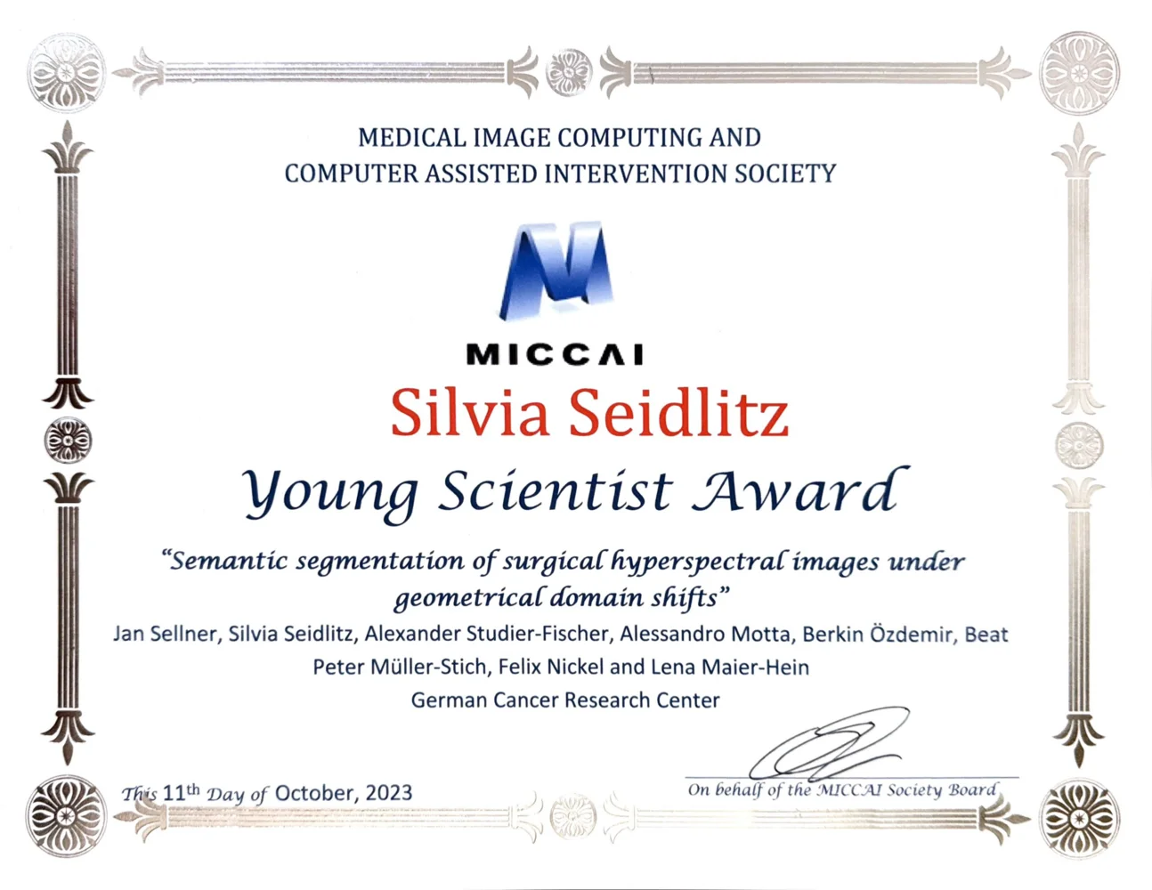 A certificate awarded to Silvia Seidlitz for the Young Scientist Award by the Medical Image Computing and Computer-Assisted Intervention Society. The award recognizes her work on "Semantic segmentation of surgical hyperspectral images under geometrical domain shifts," dated October 11, 2023.