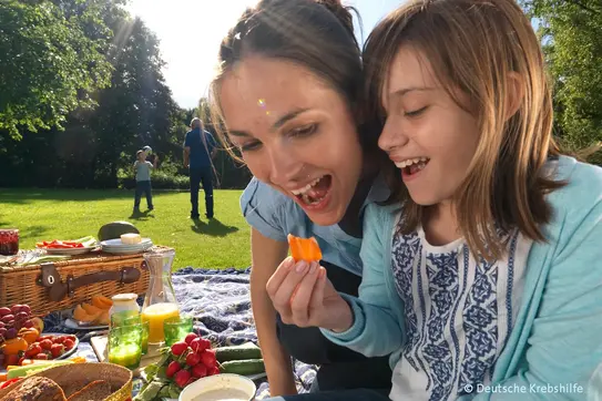 Frau und Mädchen genießen gemeinsam frisches Gemüse beim Picknick im Park.