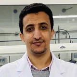 Ein Mann in einem Labor mit einem weißen Laborkittel steht vor einer Gruppe von Laborgeräten und -einrichtungen. Der Hintergrund zeigt eine sterile Arbeitsumgebung mit wissenschaftlichen Geräten und einer klaren Oberfläche.
