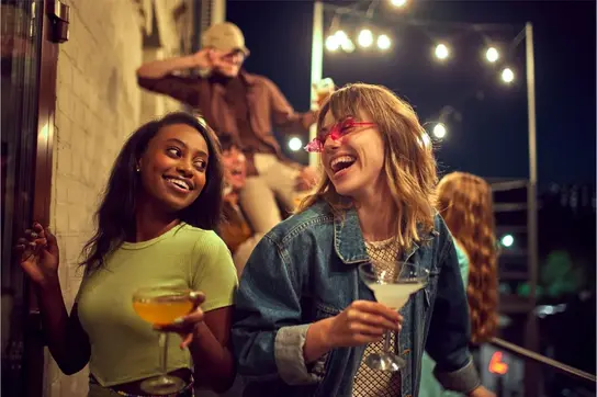 Zwei Frauen mit Cocktails in der Hand bei einer Party im Freien.