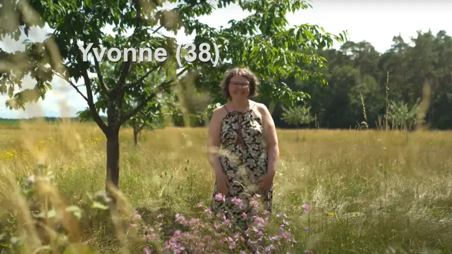 Frau im Sommerkleid steht lächelnd auf einer Wiese.