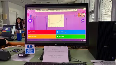 Ein Computerbildschirm zeigt eine Umfragefrage zu physikalischen Prinzipien für die Hadrontherapie mit vier möglichen Antworten. Im Hintergrund sind mehrere Personen und ein Tisch mit weiteren Computern zu sehen.