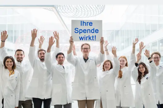 Forschungsgruppe des DKFZ hält Schild mit "Ihre Spende wirkt" nach oben.