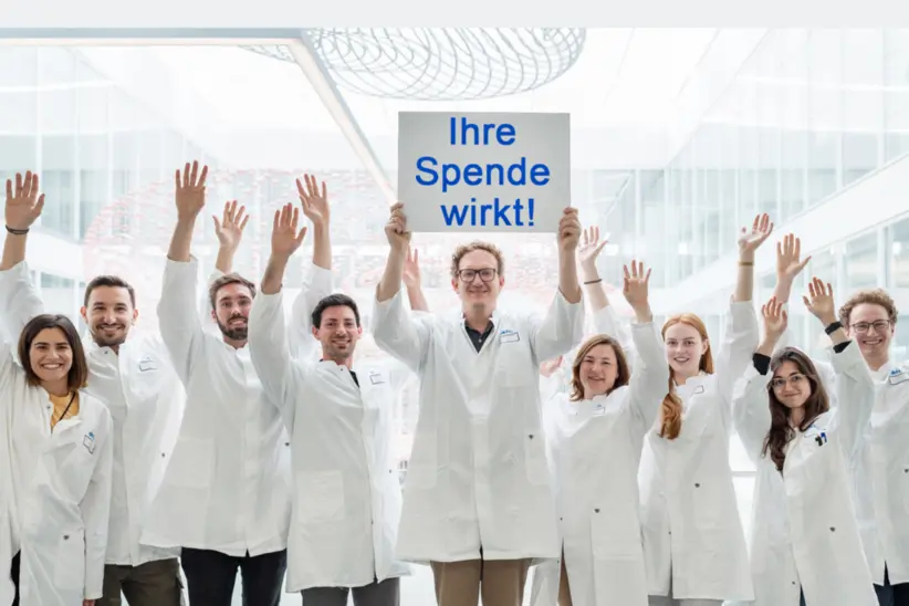 Forschungsgruppe des DKFZ hält Schild mit "Ihre Spende wirkt" nach oben.