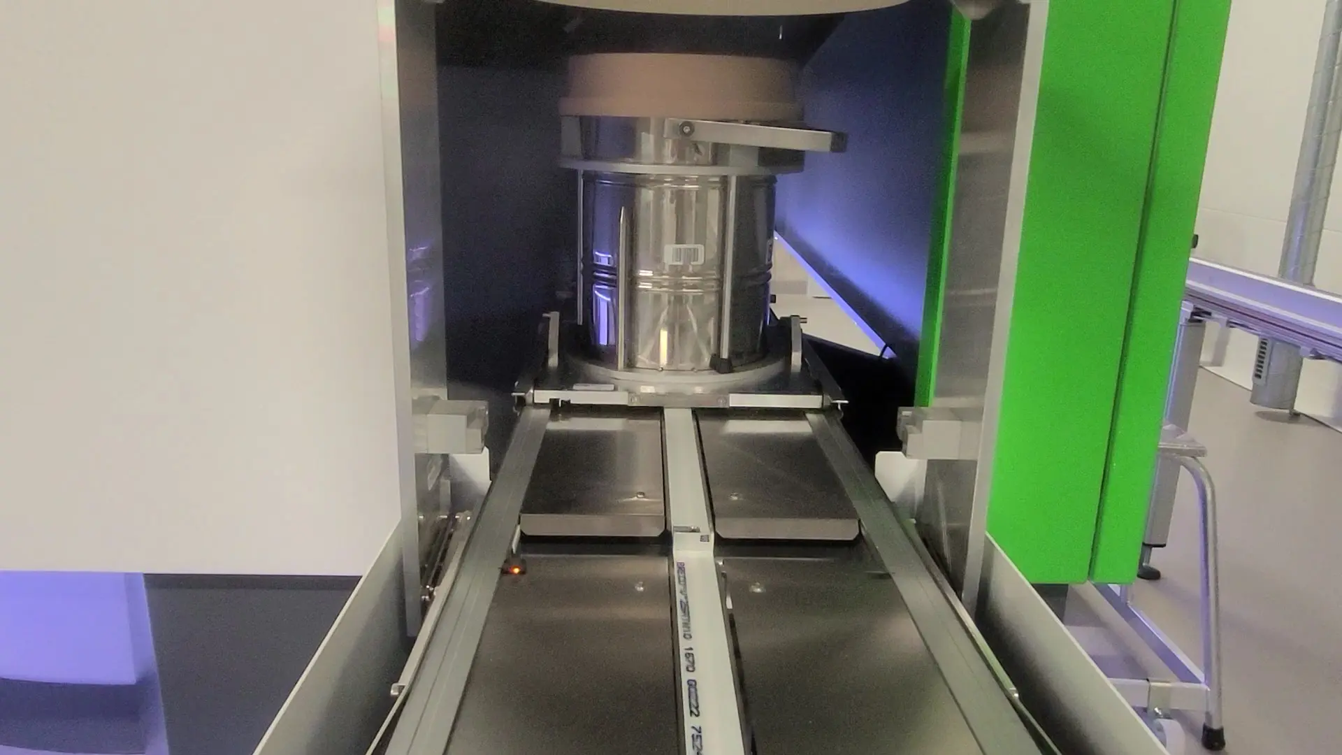 The image shows the interior of a machine designed for processing materials. A cylindrical container is positioned in the center, with a track extending outward. The machine features metallic surfaces, with some areas illuminated, suggesting a modern, industrial design focused on efficiency.