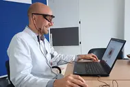 Bastian Schilling mit Eye-Tracking-Brille sitzt lächelnd am Laptop, auf dem ein Hautbild angezeigt wird.