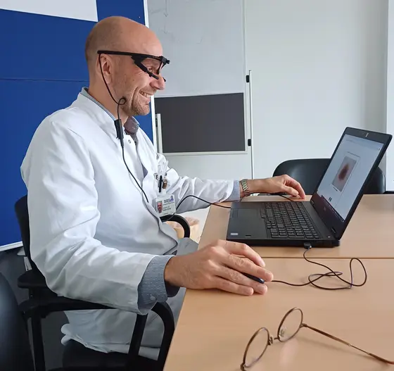 Bastian Schilling mit Eye-Tracking-Brille sitzt lächelnd am Laptop, auf dem ein Hautbild angezeigt wird.