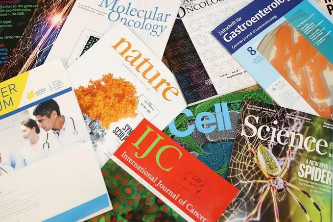 Eine Ansammlung von Fachzeitschriften über Naturwissenschaften, Medizin und Krebsforschung. Die Titel umfassen "Nature", "Cell", "Science", "Molecular Oncology" und "International Journal of Cancer". Die Zeitschriften sind farbenfroh und unterschiedlich platziert, einige zeigen auch Bilder und Grafiken.