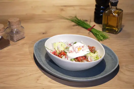 Frischer Salat mit Zartweizen, Radieschen und pochiertem Ei in einer Schale.