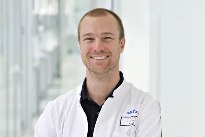 Ein Wissenschaftler in einem weißen Laborkittel steht in einem hellen, modernen Labor.