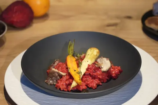 Rotes Risotto mit Wurzelgemüse und Shiitake-Pilzen in einem schwarzen Teller.