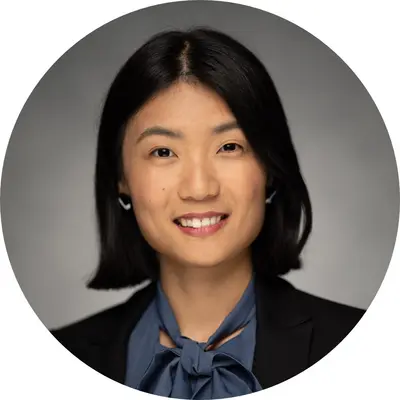 Professional headshot of Tuyu Zheng, featuring a woman with shoulder-length black hair and wearing a dark blazer and blue blouse. She has a friendly smile and is positioned in a circular frame against a neutral background.